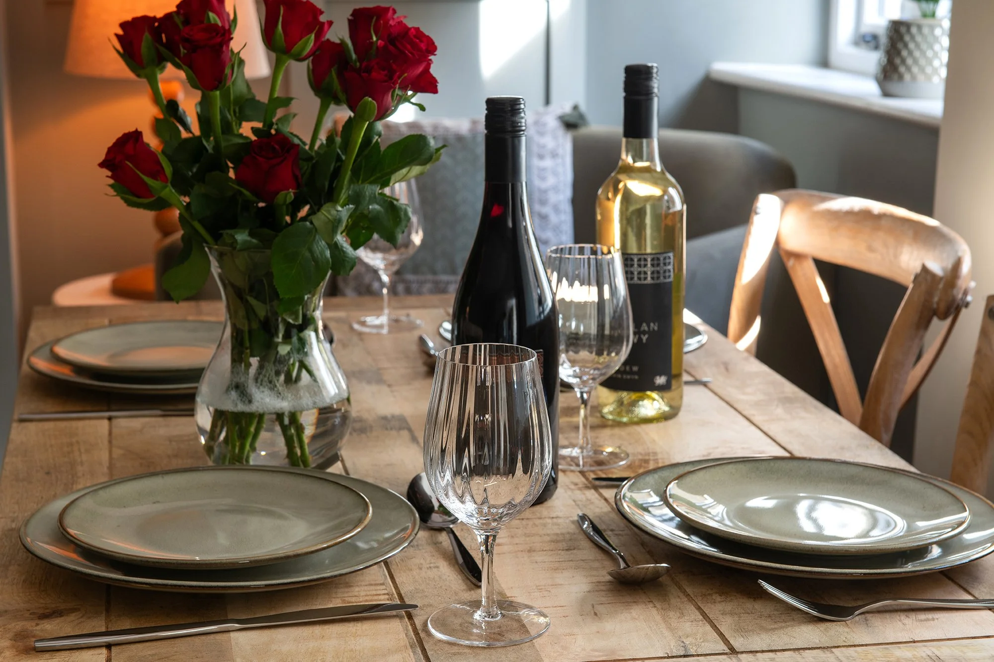 A beautifully set dining table with wine glasses, a wine bottle, and a vase of red roses, prepared for an elegant meal