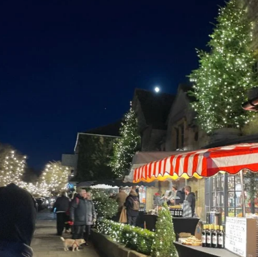 A festive evening scene on Broadway High Street featuring a lively Christmas market with illuminated trees and stalls