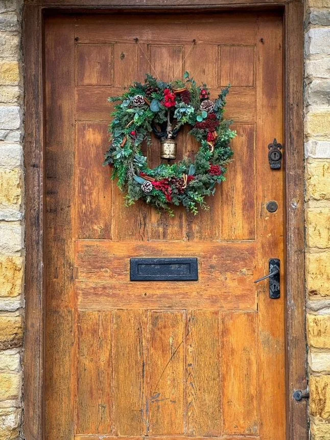 A festive Christmas wreath hanging on a rustic wooden door, capturing the holiday spirit in the Cotswolds