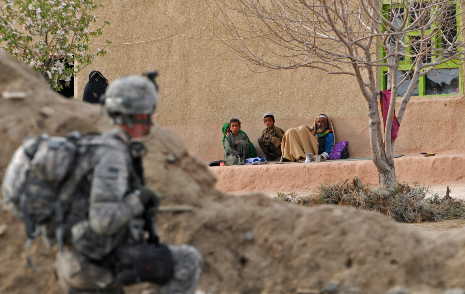  AUS soldier from 1st Platoon Alpha Company 3-187 3BCT 101 Airborne takes position as an Afghan family look at him from their house during a patrolling in Yosef Khel district of Paktika province on April 1, 2010. Orphans carry their chairs to prepare