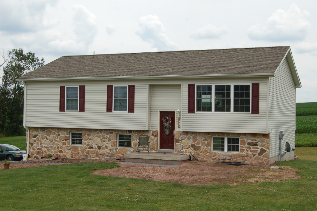 Bi-level Home Featuring a hand laid Stone Foundation covering. Concrete Front Porch. Front Door Painted to Match Shutters.
