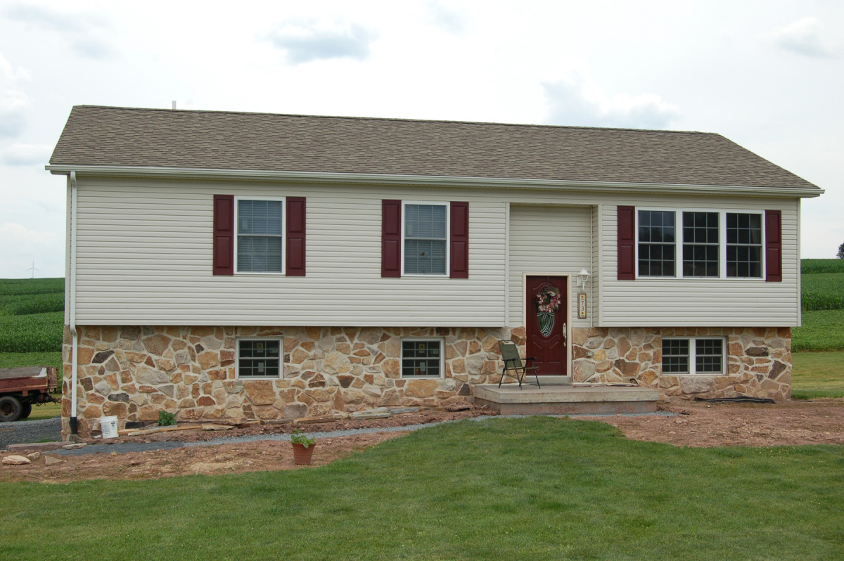 Bi-level Home Featuring a hand laid Stone Foundation covering. Concrete Front Porch. Front Door Painted to Match Shutters.