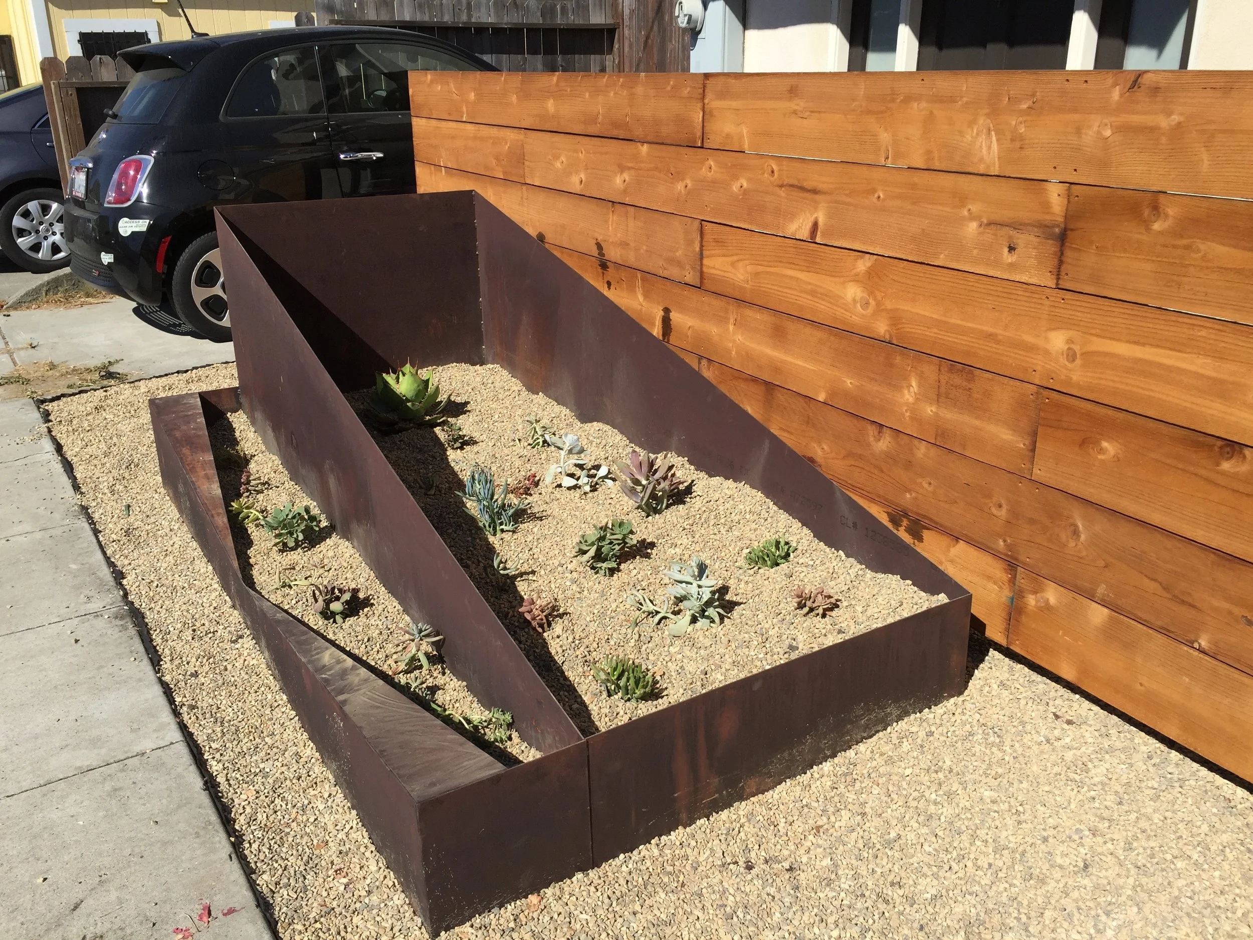 Corten Angled Planter Box This uniquely-styled angular planter box provides a haven for the succulents growing inside.