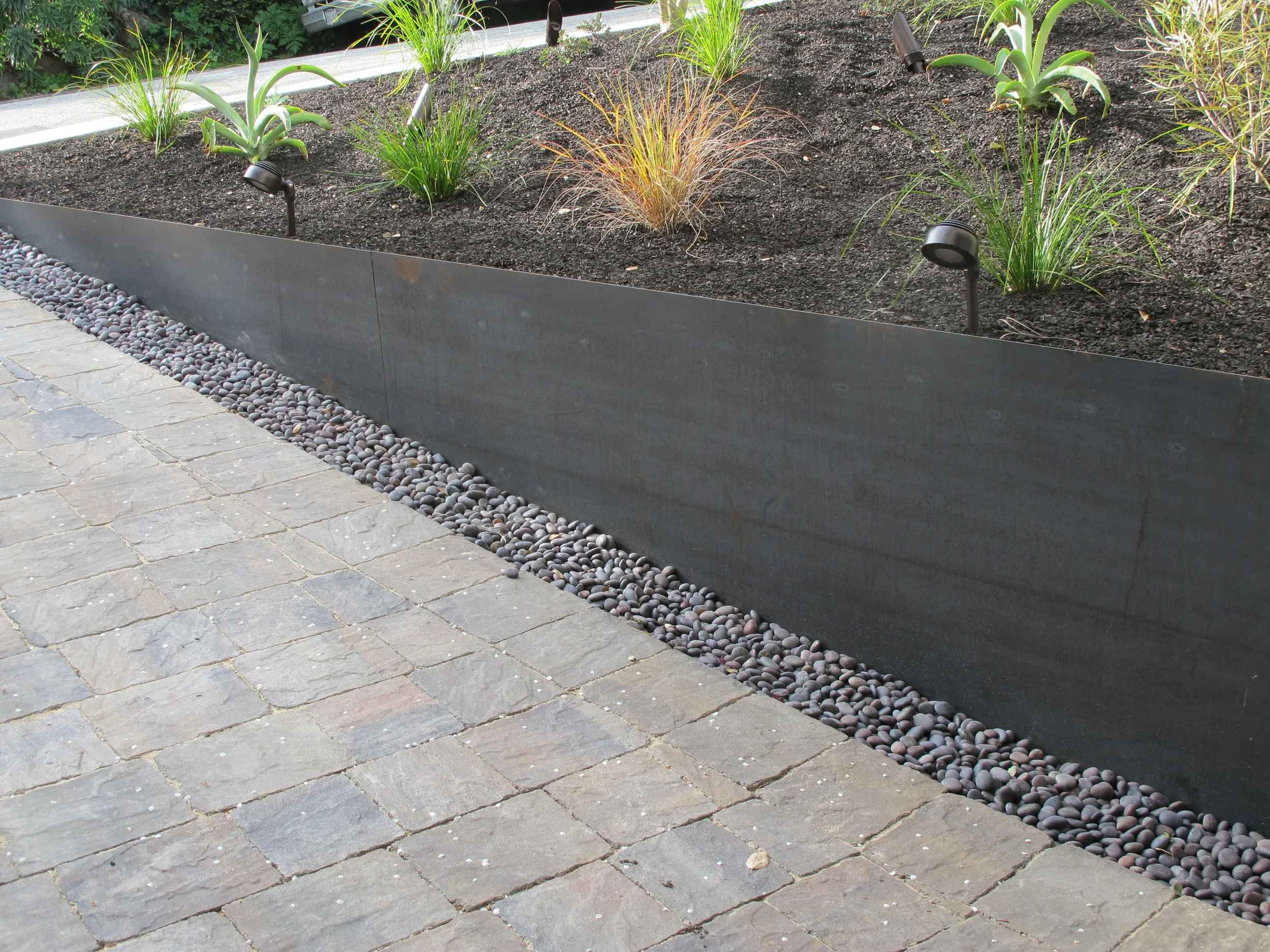 Cor-Ten Steel Retaining Wall This retaining wall transformed an Oakland Hills client's front yard and driveway as part of a major landscape renovation. Made of Cor-Ten weathering steel, this piece was both decorative and functional. The steel bolted on to a new wooden retaining wall, providing an understated, modern appearance. Designed by Chris Ford, landscape architect.
