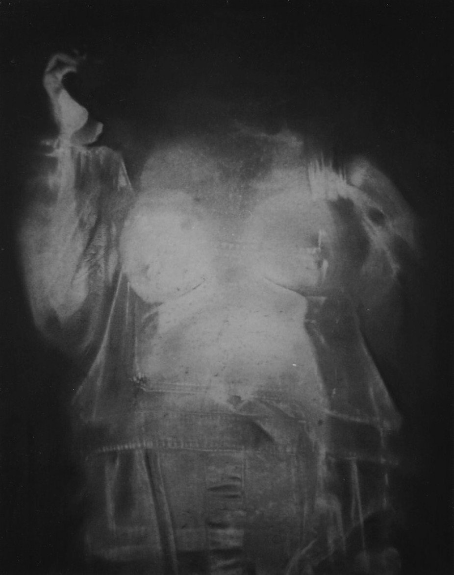 Ghostly charcoal bodyprint of a standing figure on tracing paper, with the torso, clothing and raised hand partially visible.