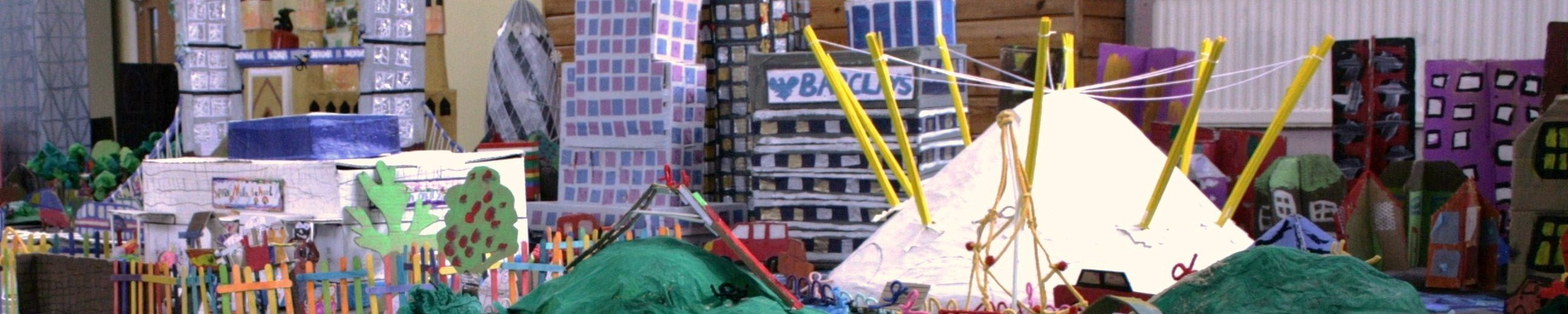 Colourful collaborative model city of London made by children, featuring buildings, trees, playgrounds, tents and connecting structures.