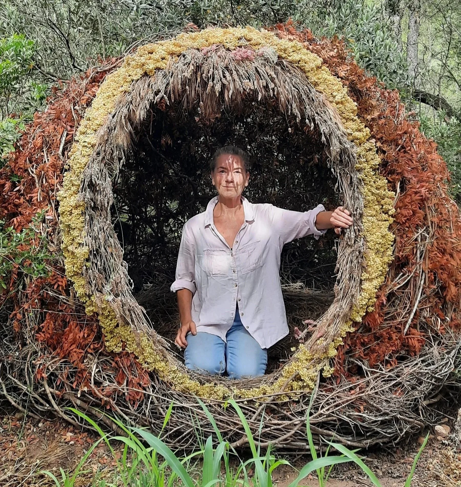 Artist Laura Williams standing within the circular entrance of her woven woodland sculpture Casanova del Bosque in Catalonia.