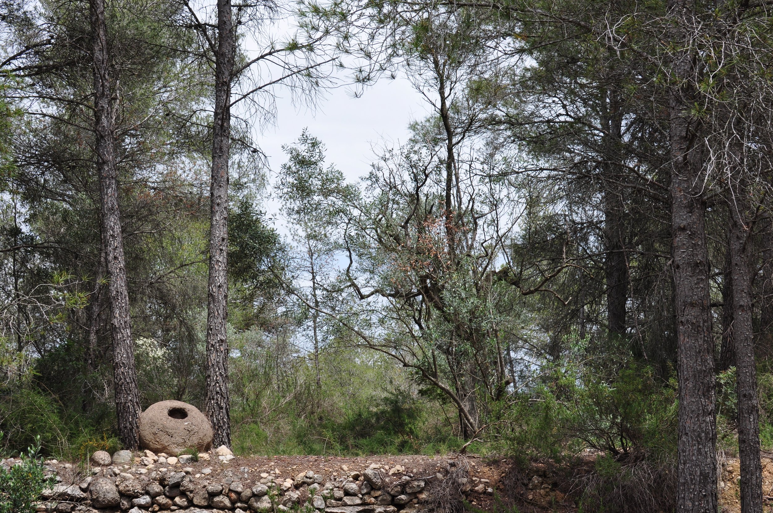Retirada, a rounded plaster sculpture with a dark circular opening, positioned among trees beside a forest path in Catalonia.