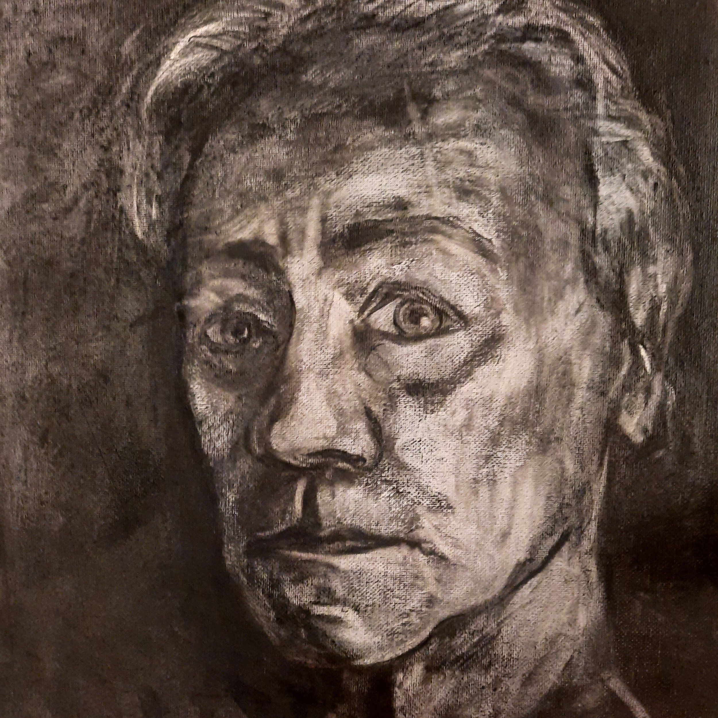 Close-up charcoal self-portrait of the artist looking directly towards the viewer, drawn with strongly contrasted gestural marks.