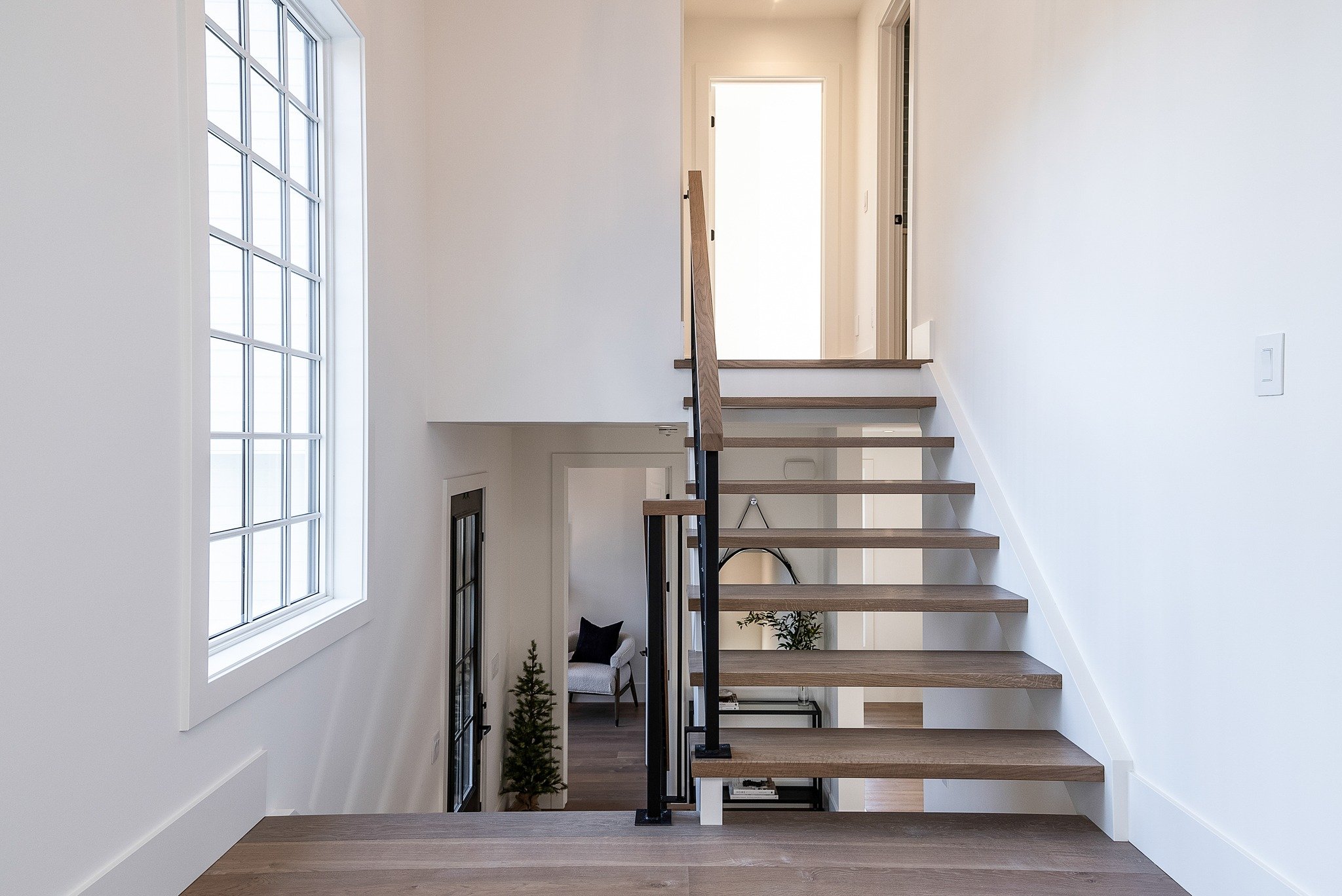 This raised bungalow was perfect to add a loft space above the garage. 🚪 Upon entering you are greeted by open rise, white oak stairs which lead you past a beautiful window and into the loft. The sloped ceilings, elongated hearth, and exposed timber