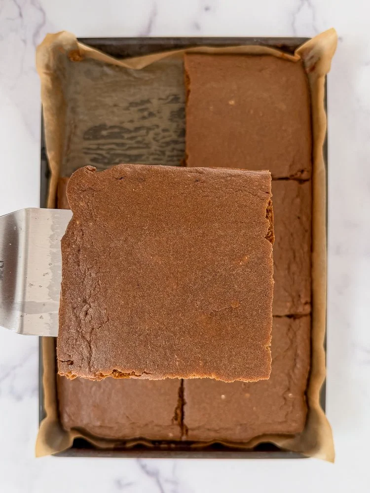 Close up of a slice of sheet pan gingerbread pancakes over the rest of the baking pan which is resting on a marble kitchen counter.