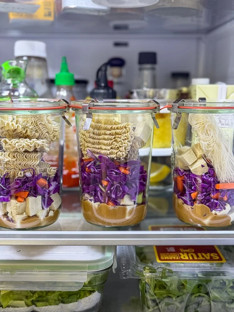 Line up of instant noodle meal prep jars on a refrigerator shelf being stored for later use.