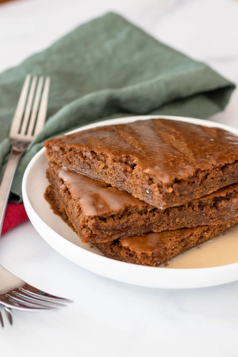 Stack of high protein sheetpan gingerbread pancakes on a plate drizzled with a simple glaze, with forks and Christmas napkins.