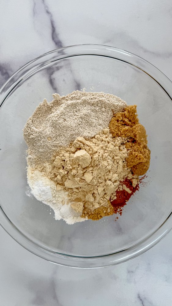 Dry ingredients, inclusion plant based protein powder in a bowl to make high protein gingerbread sheet pan pancakes.