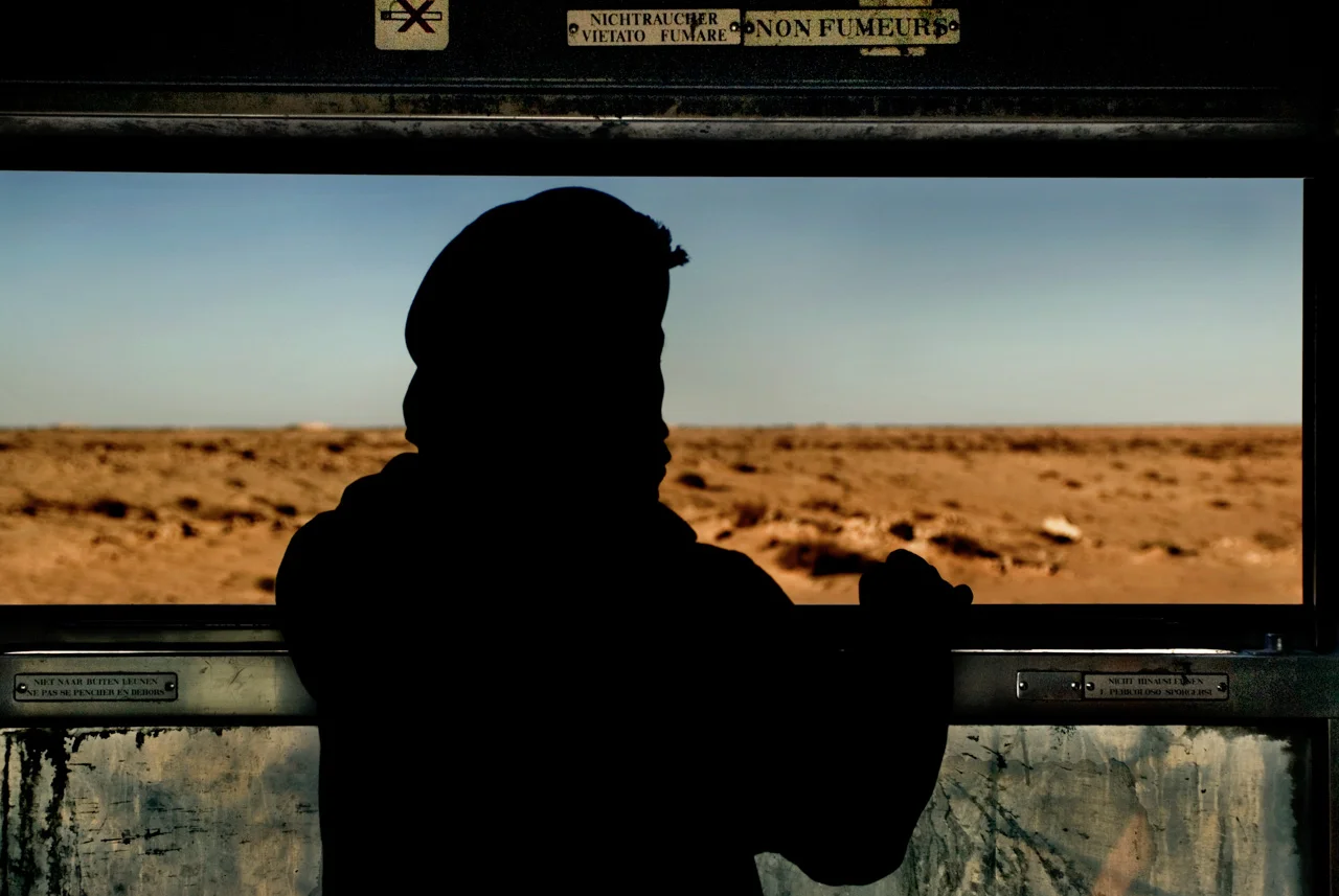Ogni giorno il treno attraversa il deserto della Mauritania per collegare Zouerat - città mineraria del Sahara settentrionale scoperta negli anni venti dai francesi - a Nouadibou, crocevia di pescherecci, di merci e di migranti affacciato sull'Atlantico. Diciotto ore il viaggio sui seicentocinquanta chilometri di binari che attraversano la distesa di sabbia.
Ogni tipo di mercanzia aspetta di trovare il suo posto sui vagoni e quando il treno arriva c'è già chi lancia, chi afferra e chi carica. Sacchi che salgono, mani che scendono: lo sforzo collettivo di una folla indisciplinata in cui tutti prendono posto, montoni e capre compresi.