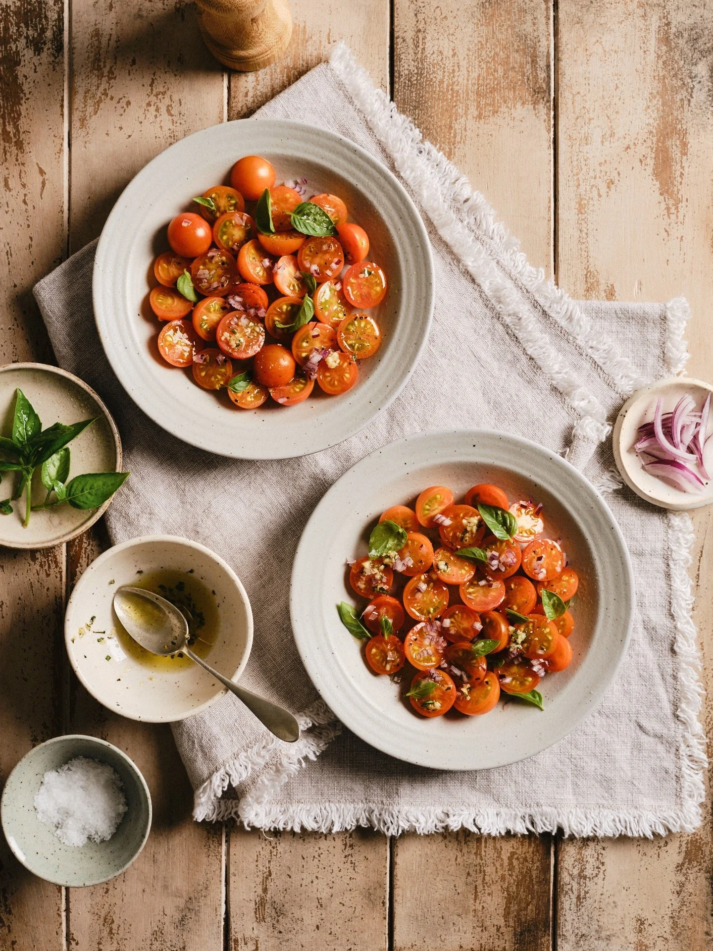 Two plates with orange cherry tomatoes, garnished with red onions and basil leaves