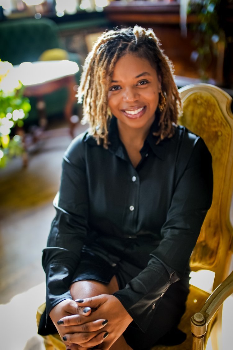 Photo of Theodosia Cook smiling, wearing a black dress seated in a wooden chair