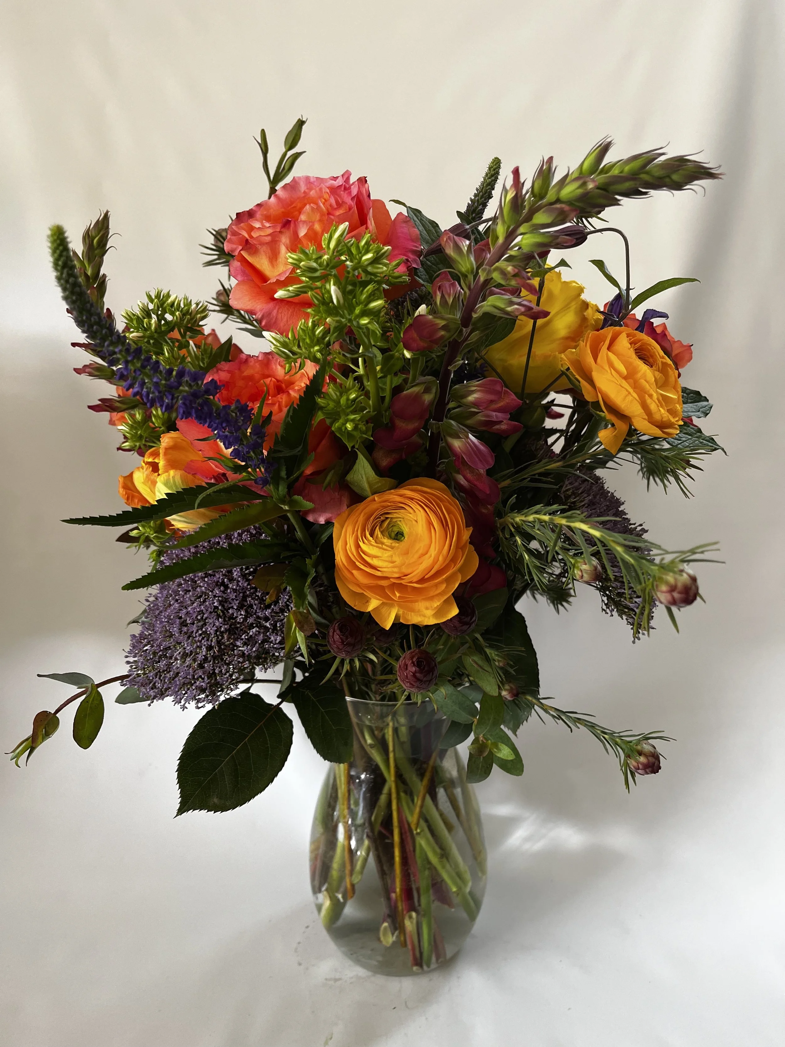 Fresh floral arrangement with orange ranunculus, eucalyptus and mixed foliages by Snowdrops & Sage