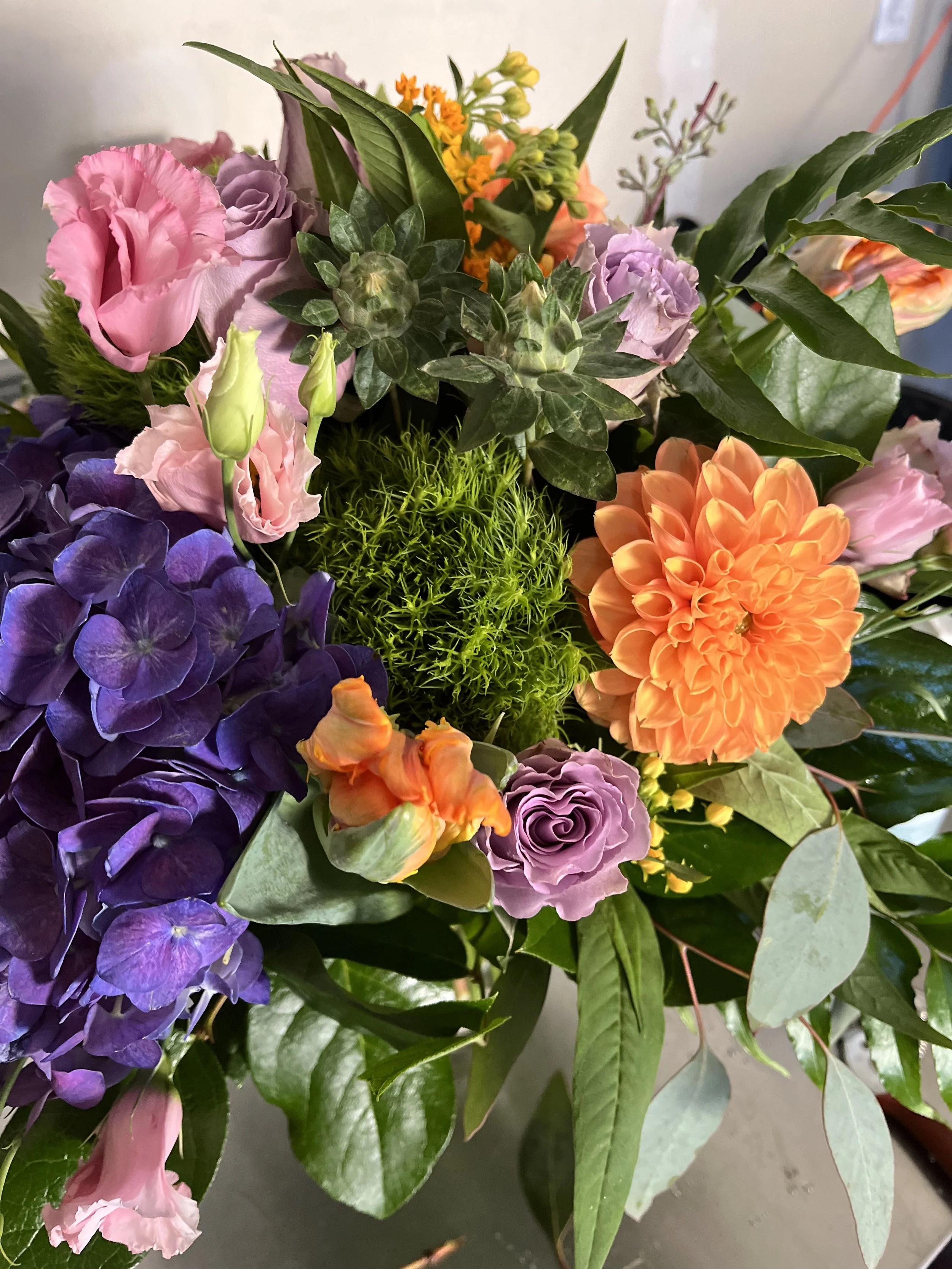 Floral arrangement from Snowdrops & Sage featuring a mix of pink roses, purple hydrangeas, and orange dahlias