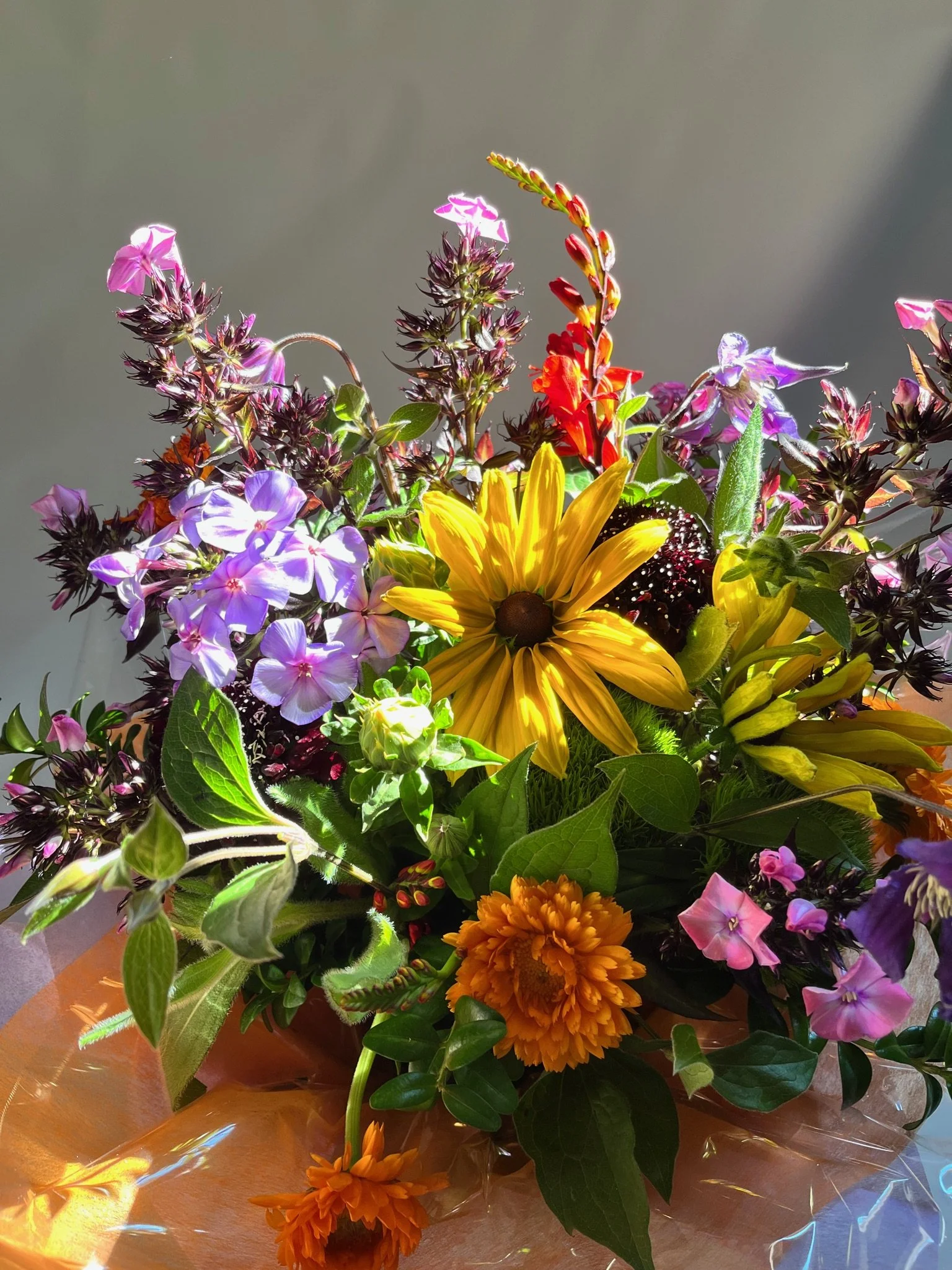 Colorful flower bouquet with yellow, purple, orange, and red blooms against a gray background.