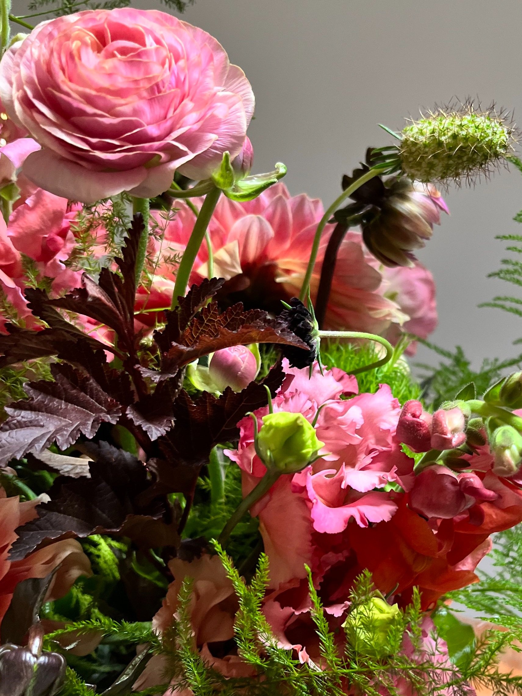 Close-up of a vibrant floral arrangement featuring pink ranunculus, roses, and various green foliage.
