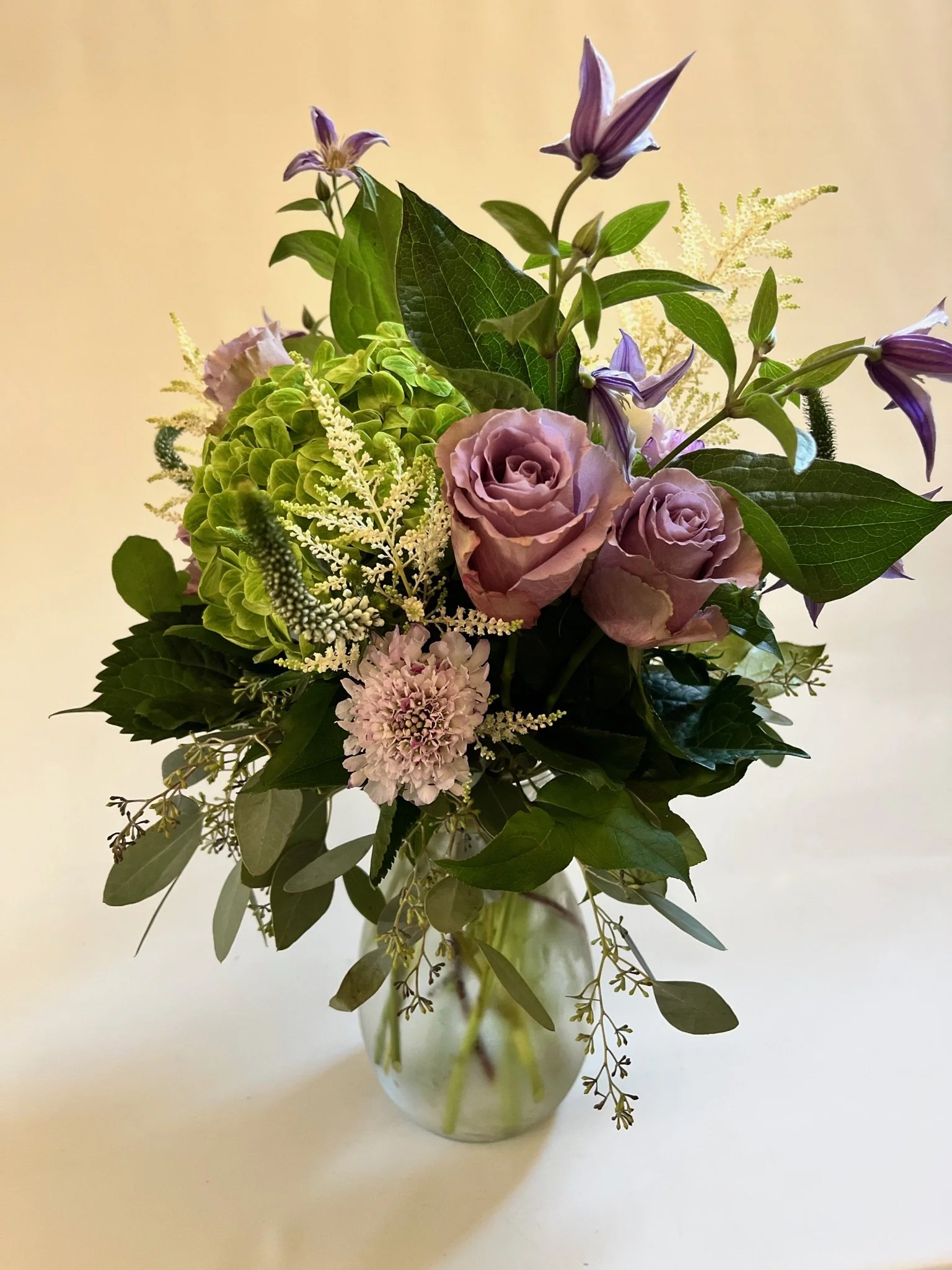 Floral bouquet with dancing lavender clematis, emerald hydrangeas, and delicate greenery by Snowdrops & Sage