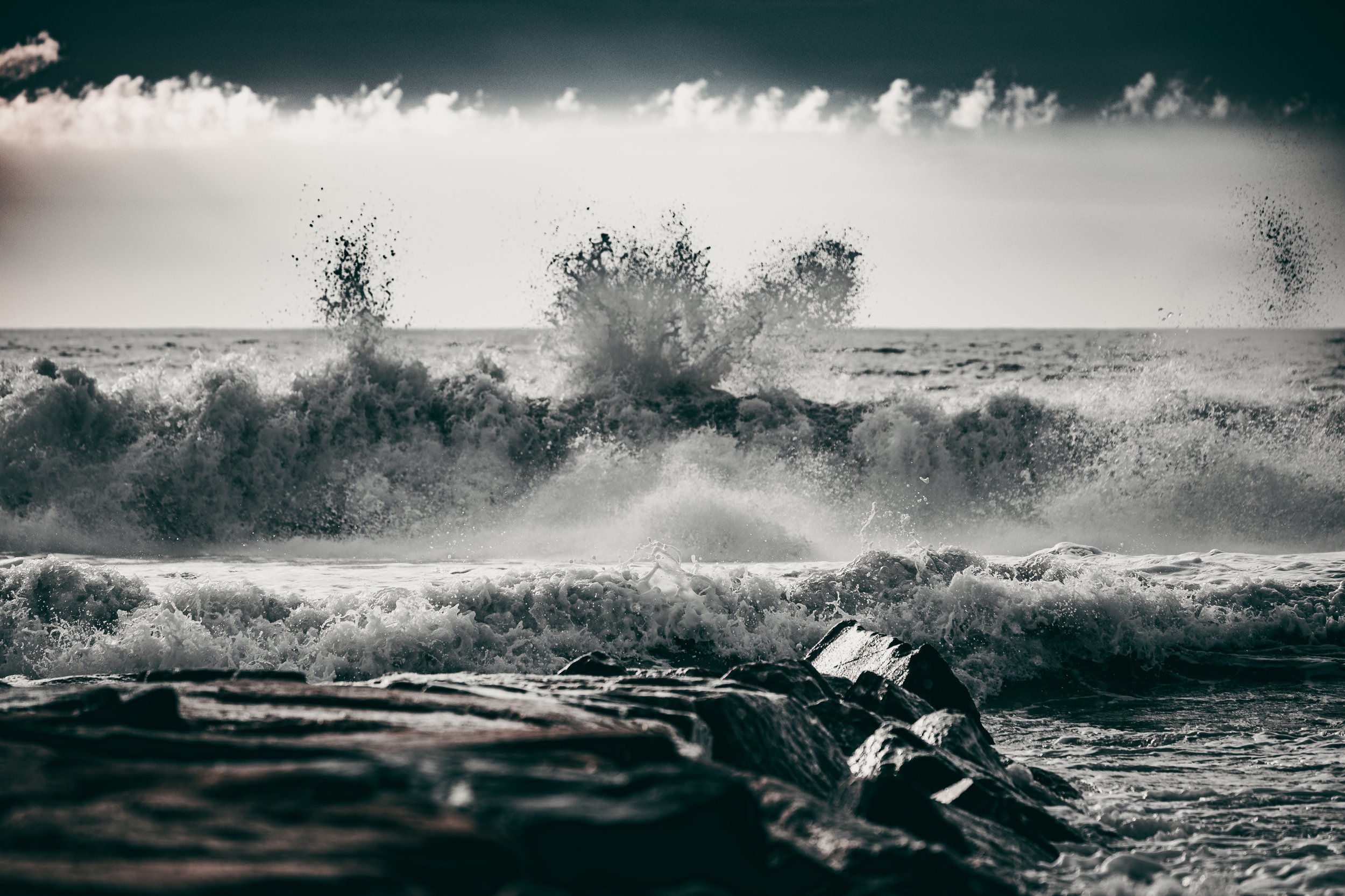 Waves crashing on the rocks at the coast, with dark clouds above and a moody atmosphere.