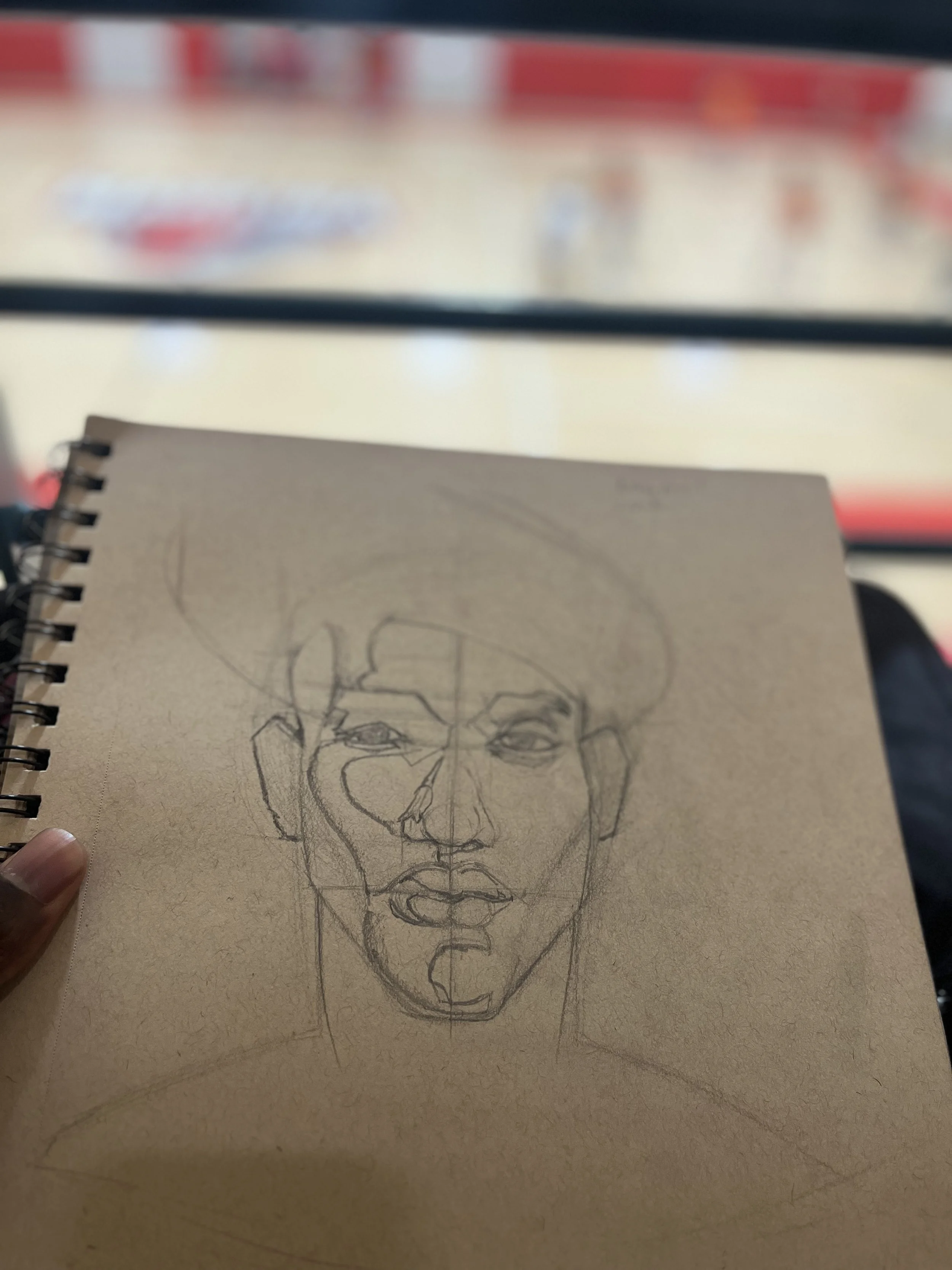 Sketch of a woman's face on a brown notebook held by a person's hand, with a blurry store interior in the background.