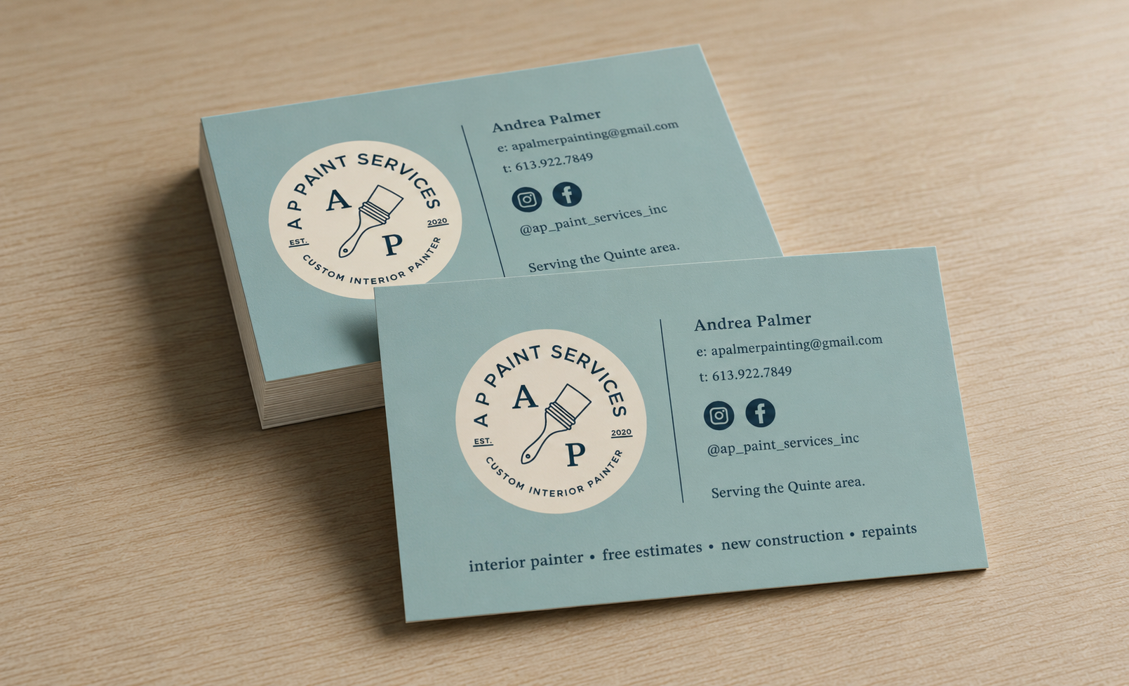 Business cards for 'A Paint Services,' featuring a logo with a paintbrush and text, with contact information and social media icons on a wooden surface.