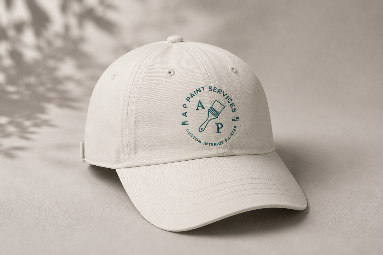A white baseball cap with a logo that says 'A Paint Services' with a paintbrush graphic in the center, and the text 'EST. 2020' and 'Custom Interior Painter' on it.