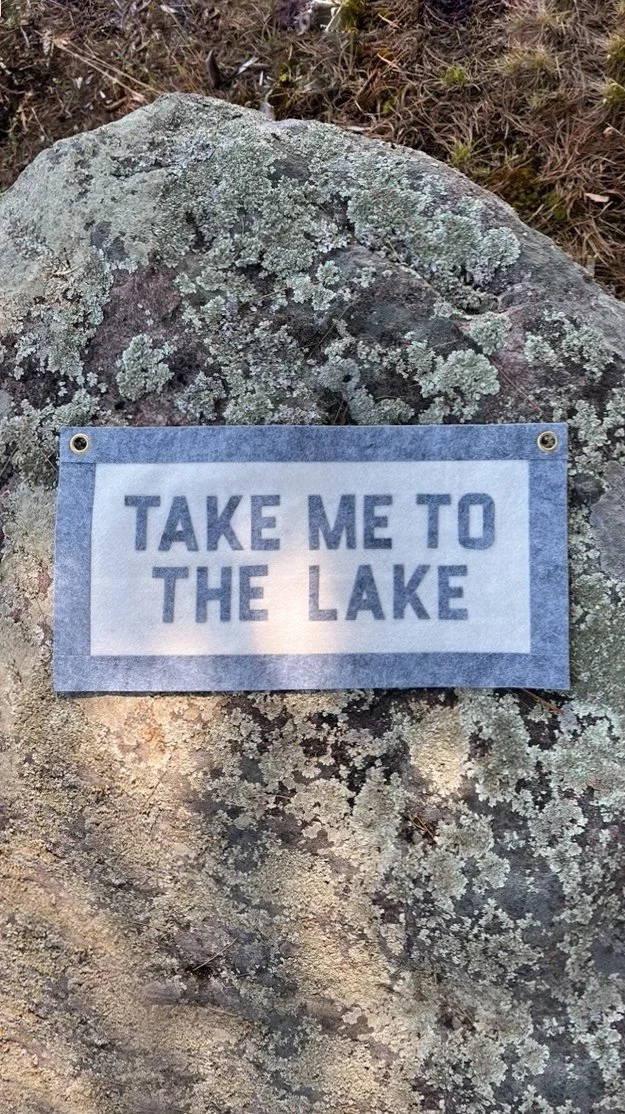 A rock with moss and lichen growth, with a note attached reading 'Take me to the lake'.