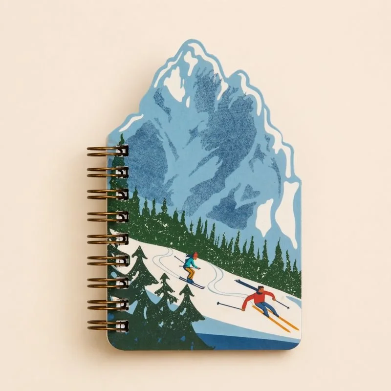 Notepad with a colorful mountain and skiing scene illustration, featuring skiers and pine trees.