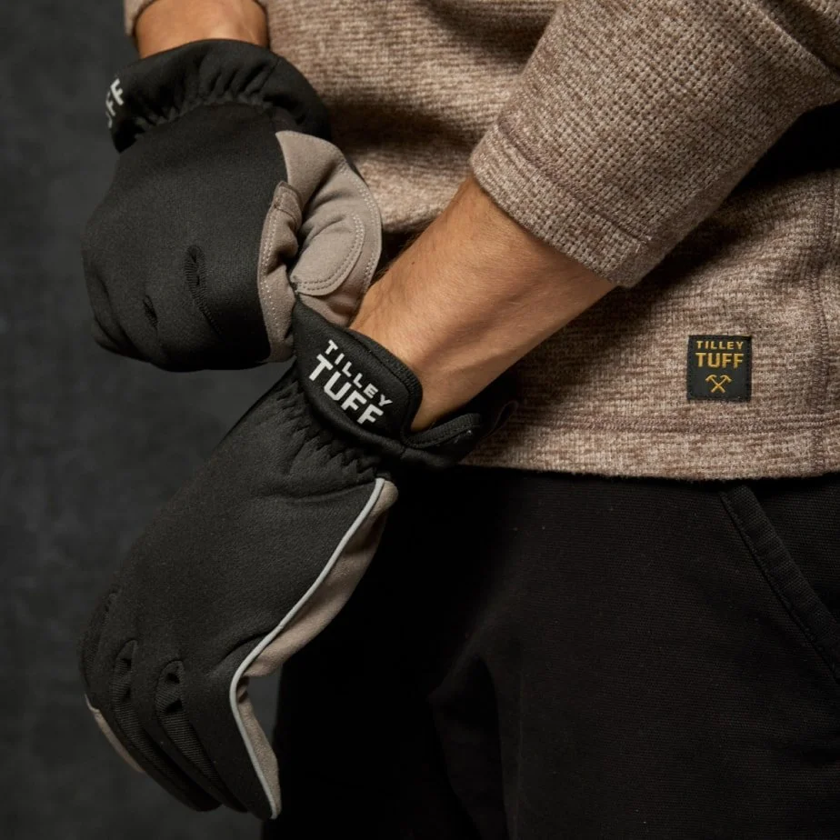 Person wearing Tilley Tuff gloves with black and beige fabric, standing against a dark background, adjusting the gloves.