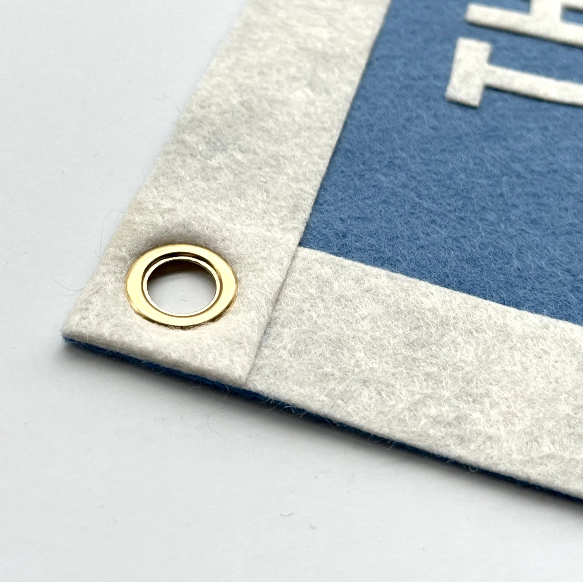 Close-up of a felt-tip marker with a brass-colored metal ring near the tip, placed on a white felt piece with a blue textured paper background.