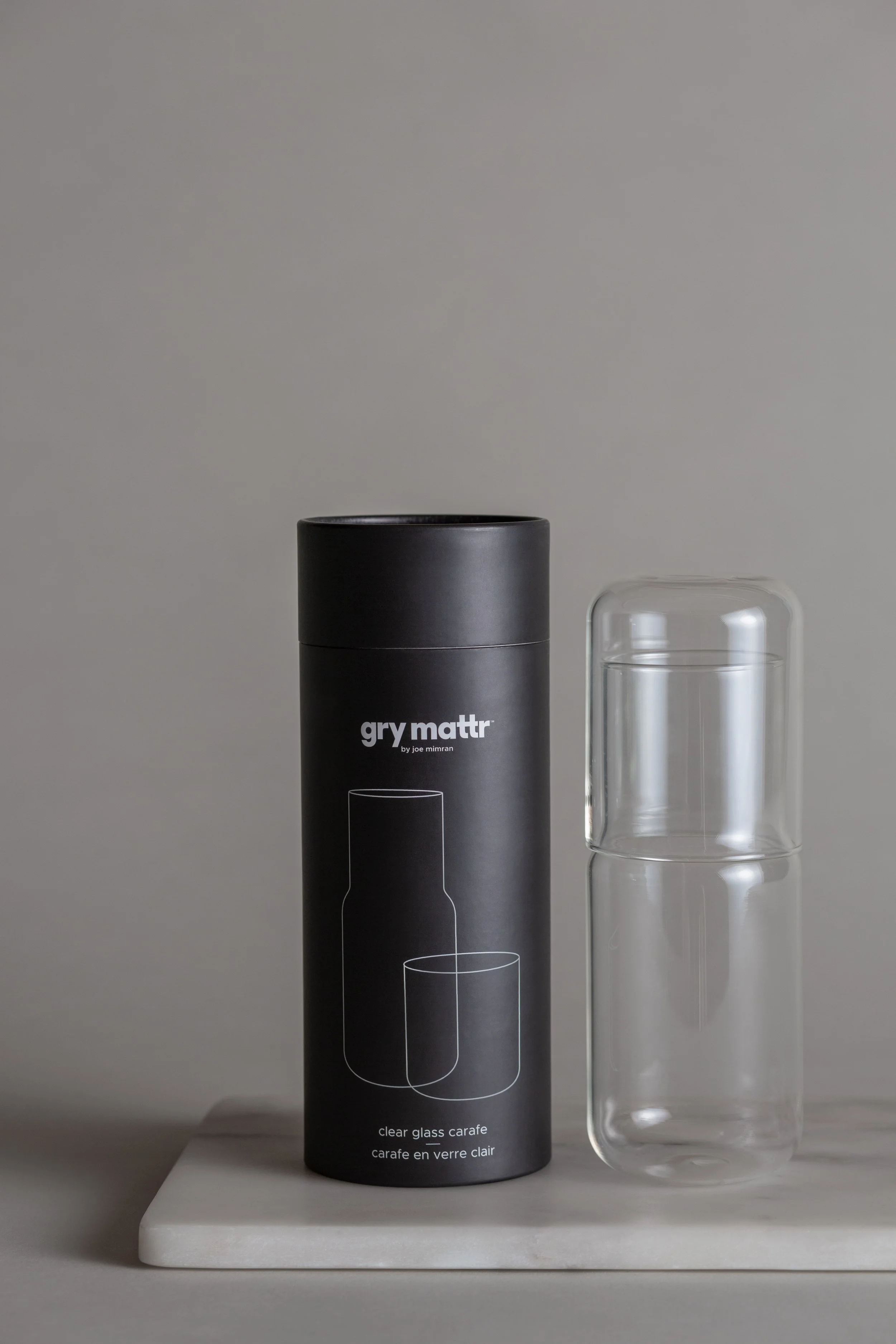 A clear glass carafe next to its black packaging box labeled 'gry mattr' and a white marble tray, all set against a light gray background.