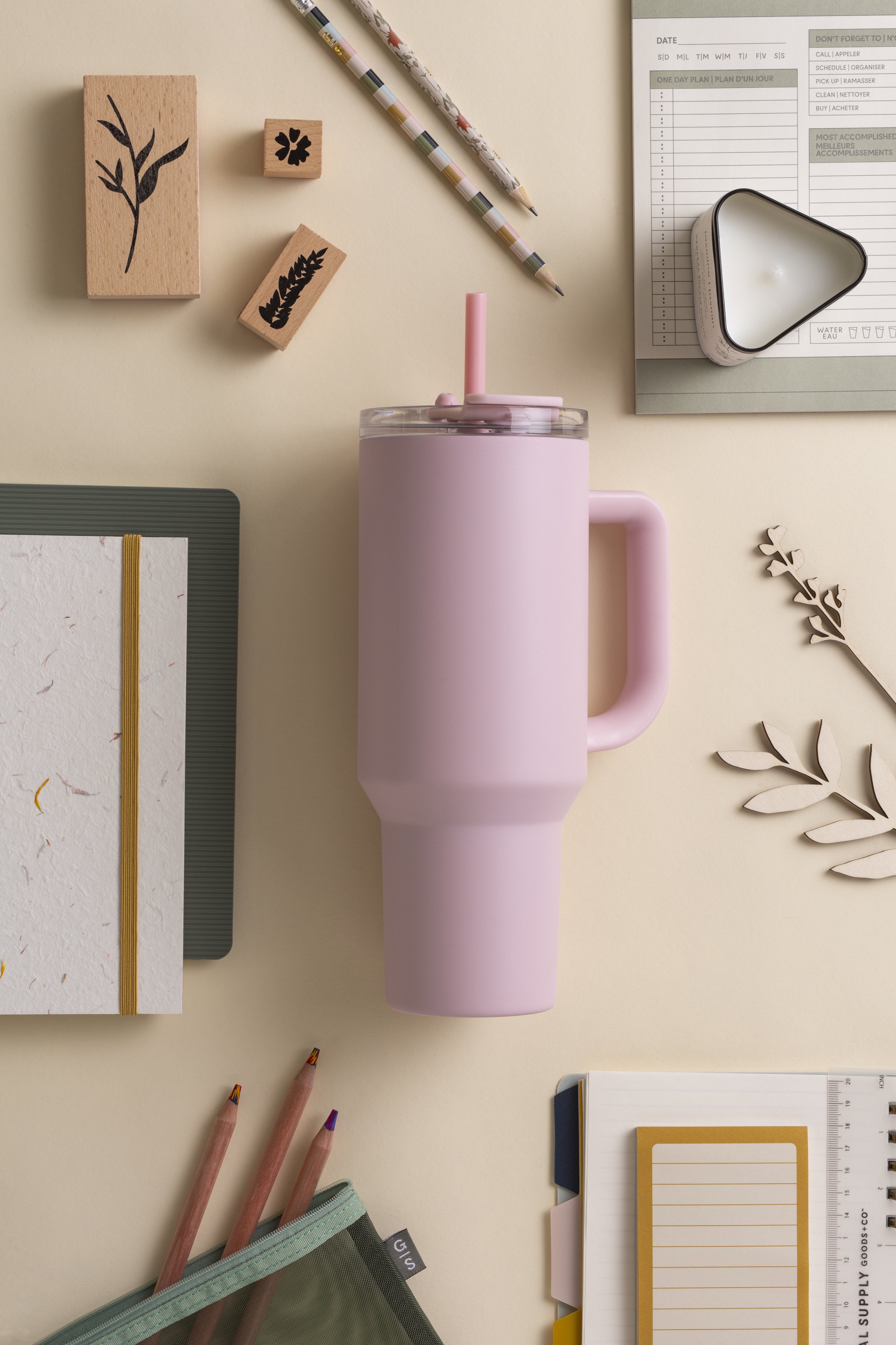 Flat lay of stationery and a pink reusable tumbler on a light-colored surface, including wooden stamps, notebooks, pens, and stationery accessories.