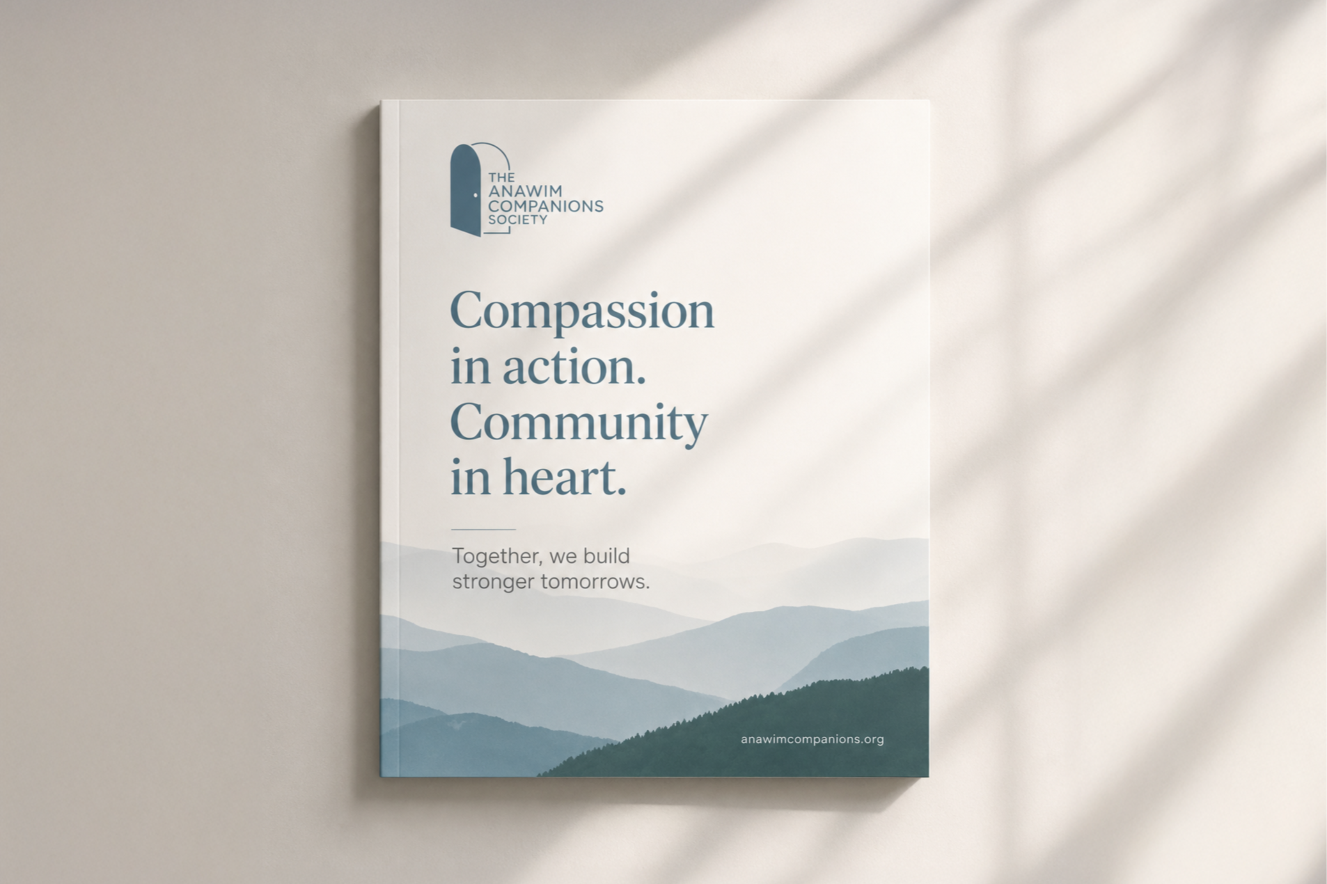 A brochure from the Anawim Companions Society featuring a landscape of blue mountain ranges. The text reads, "Compassion in action. Community in heart." and the website, anawimcompanions.org.