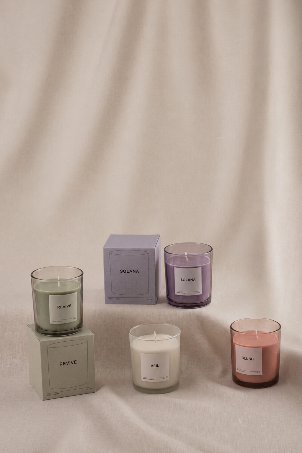 Four candles in pastel colors, labeled Revive, Veil, Solana, and Blush, with their packaging boxes on a beige fabric surface and backdrop.