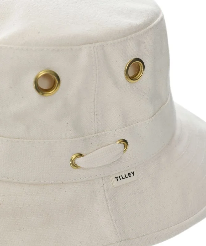 Close-up of a white Tilley bucket hat with gold eyelets and a chin strap.