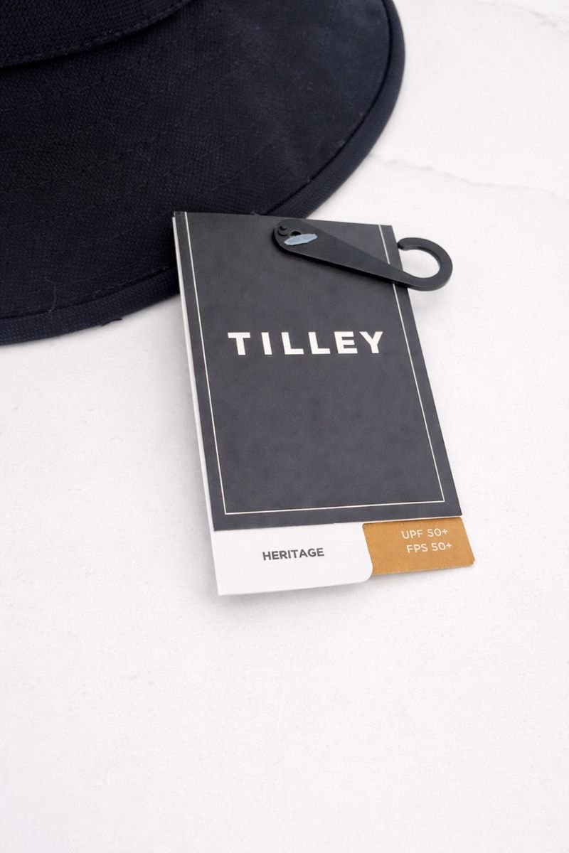 Close-up of a Tilley hat tag on a white surface with part of a black bag visible in the background.