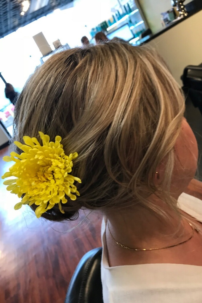 Side - Swept Flower Updo:  Everyone loves a side swept updo for a big night! This look is soft and pretty, and will gracefully frame anyone’s face . The flower in the back adds a pop of color and texture, and can be carefully matched as the perfect companion to your outfit! This floral ‘do will be sure to make you and your look stand out for a special night.
