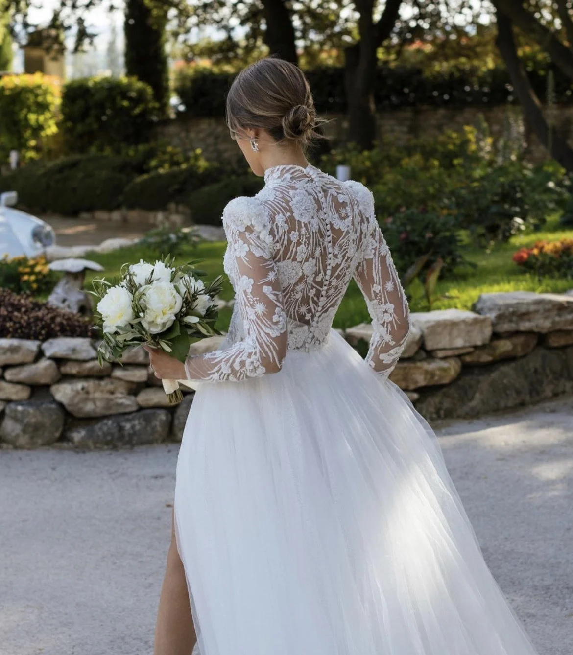 Une femme en robe de mariée avec un voile en dentelle, tenant un bouquet de fleurs blanches, dans un jardin
