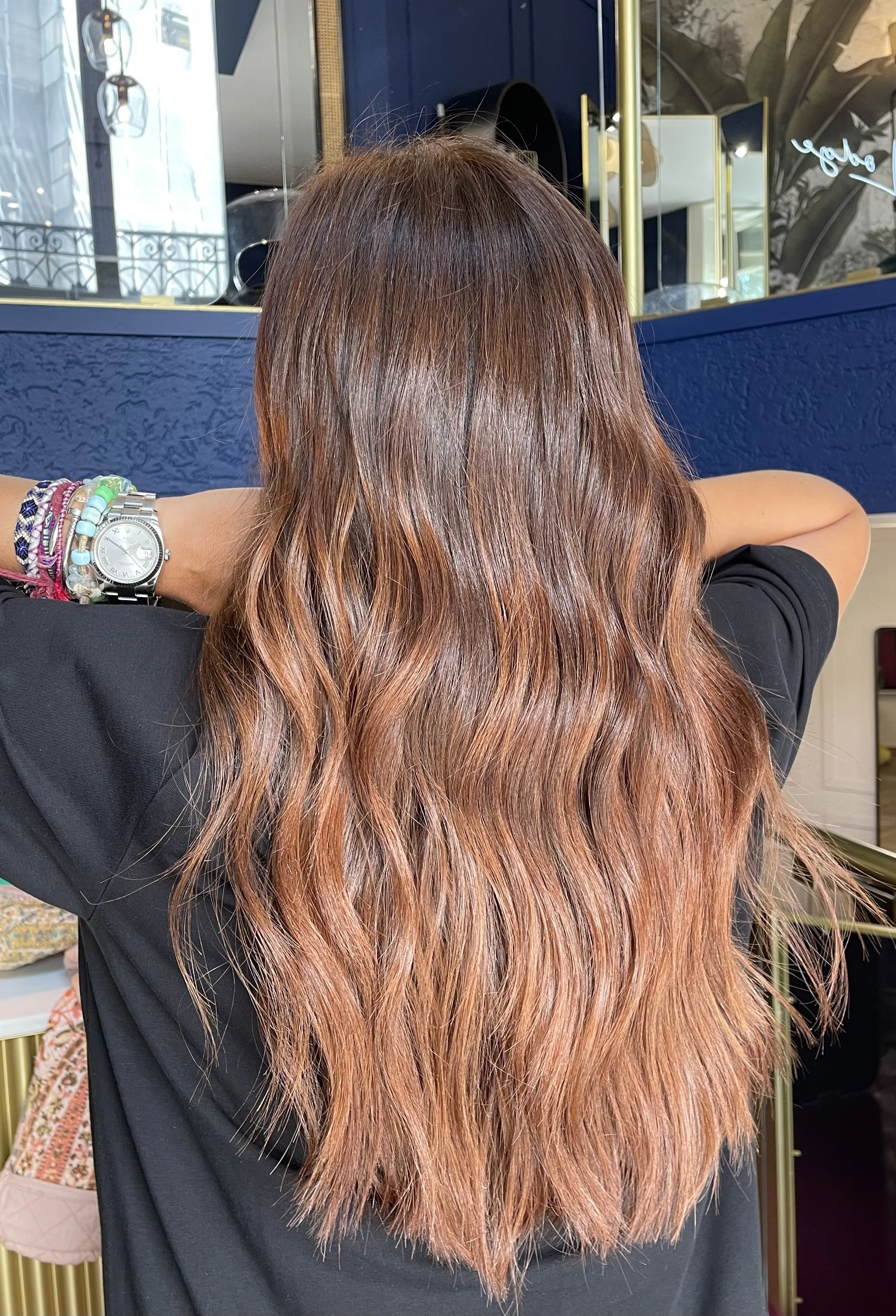 cheveux longs et ondulés de couleur cuivrée, vue de dos, portés par une personne portant un bracelet et une montre