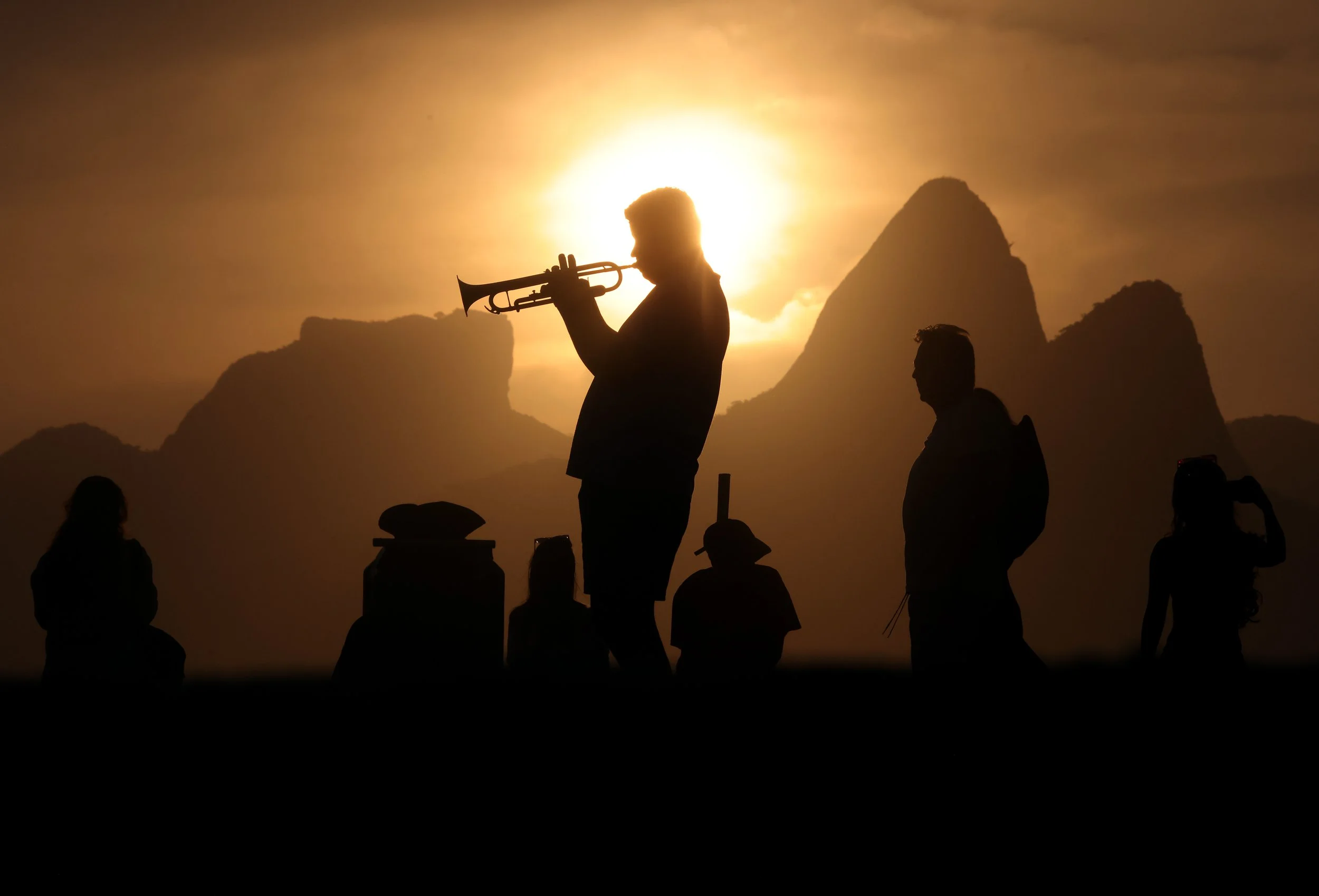 Ramon Andrade plays the trumpet on the boardwalk at Arpoador in Rio de Janeiro, as hundreds gather to watch the sunset in front of the silhouette of the iconic Two Brothers mountains.