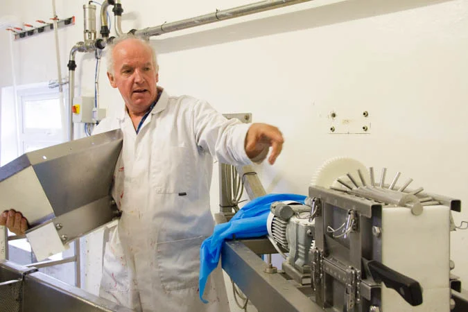 Tom took off the funnel top of the milling machine to show the mechanical magic inside. He puts the curds in, and the pegs chop them up to so they’re perfect to press into wheels.