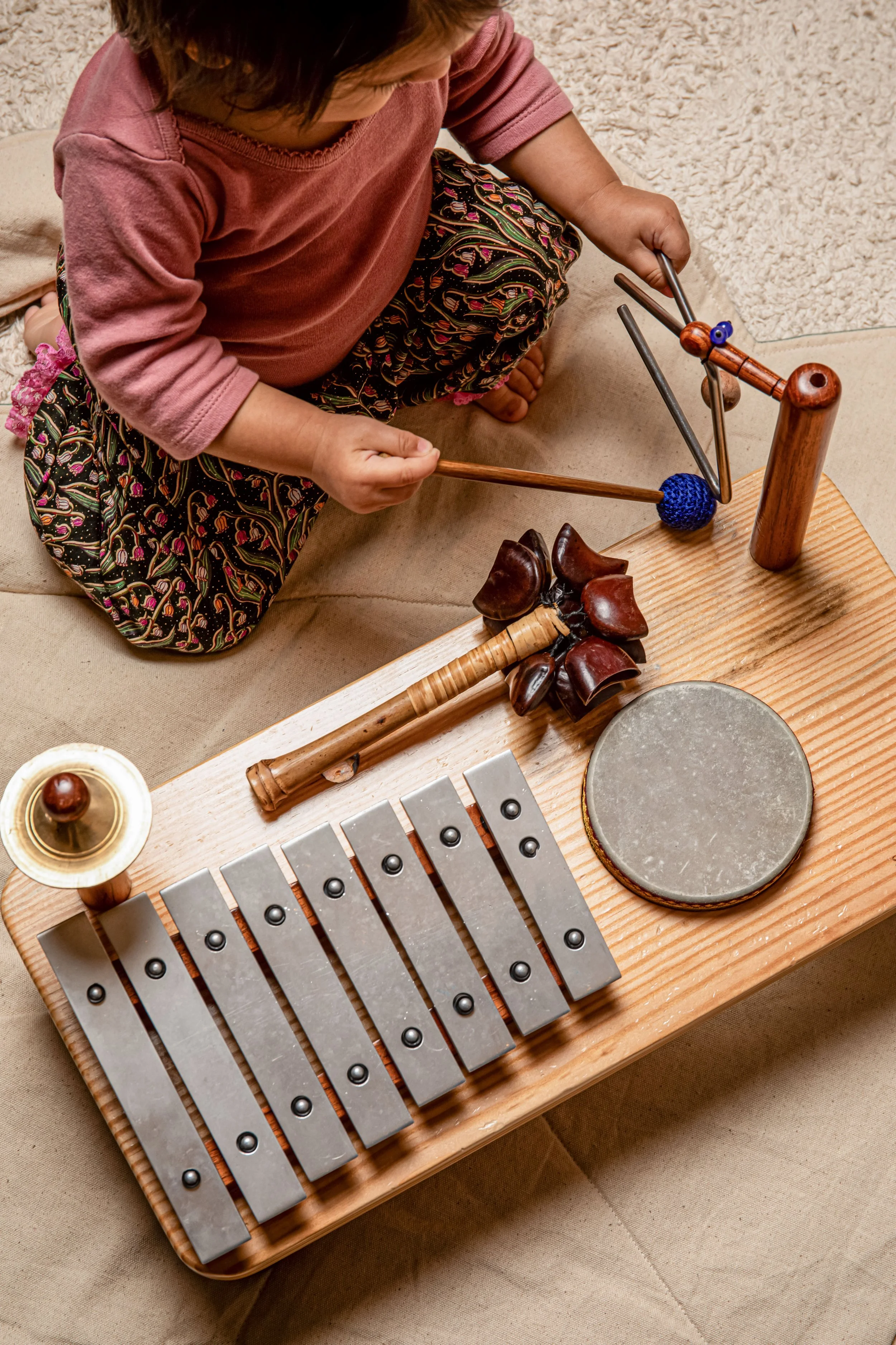 A child sitting on a beige sofa playing a wooden xylophone with metal bars and a mallet.