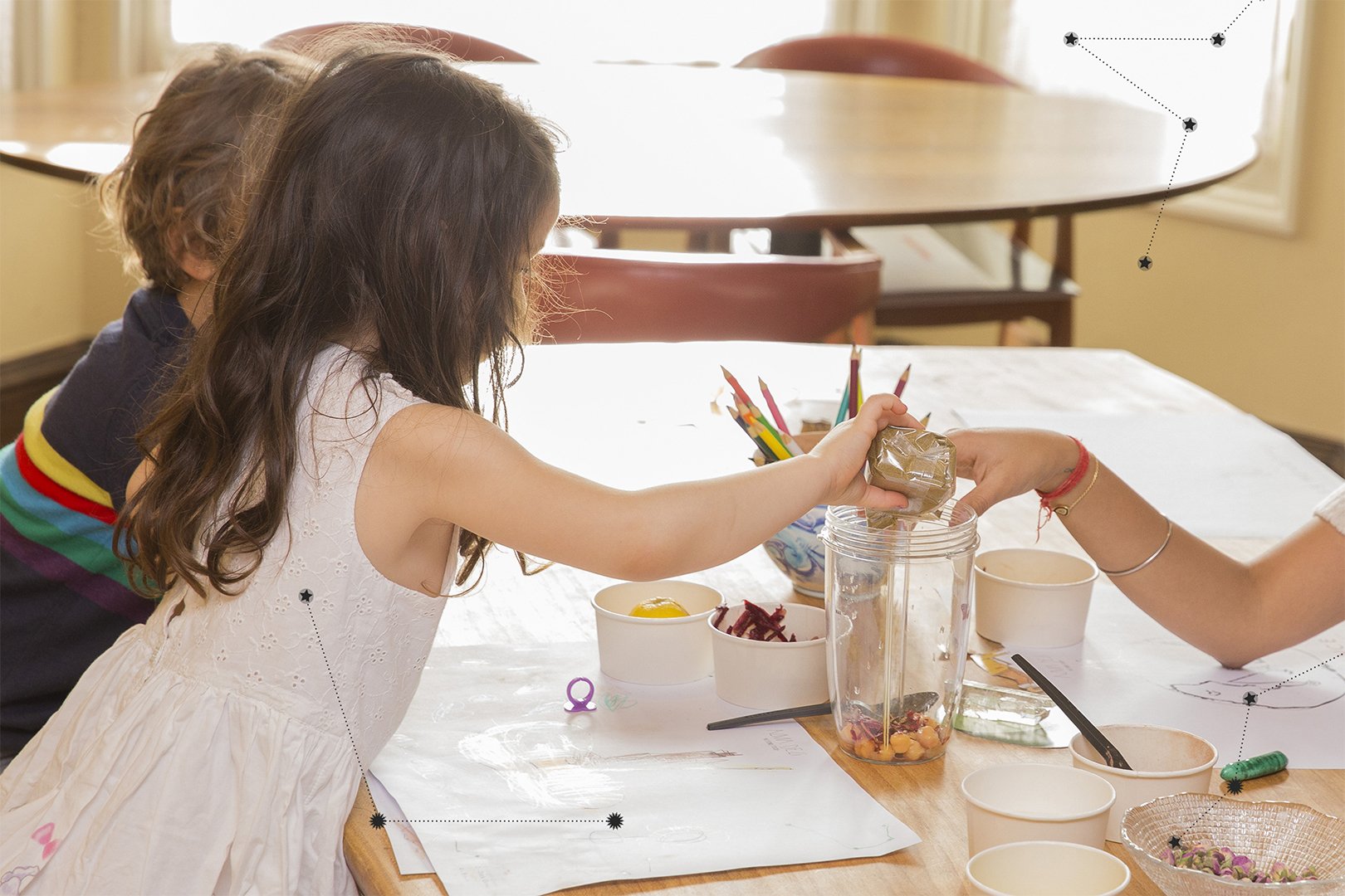 Children engaged in a creative activity at a table, pouring ingredients into a container while drawing and exploring through play.