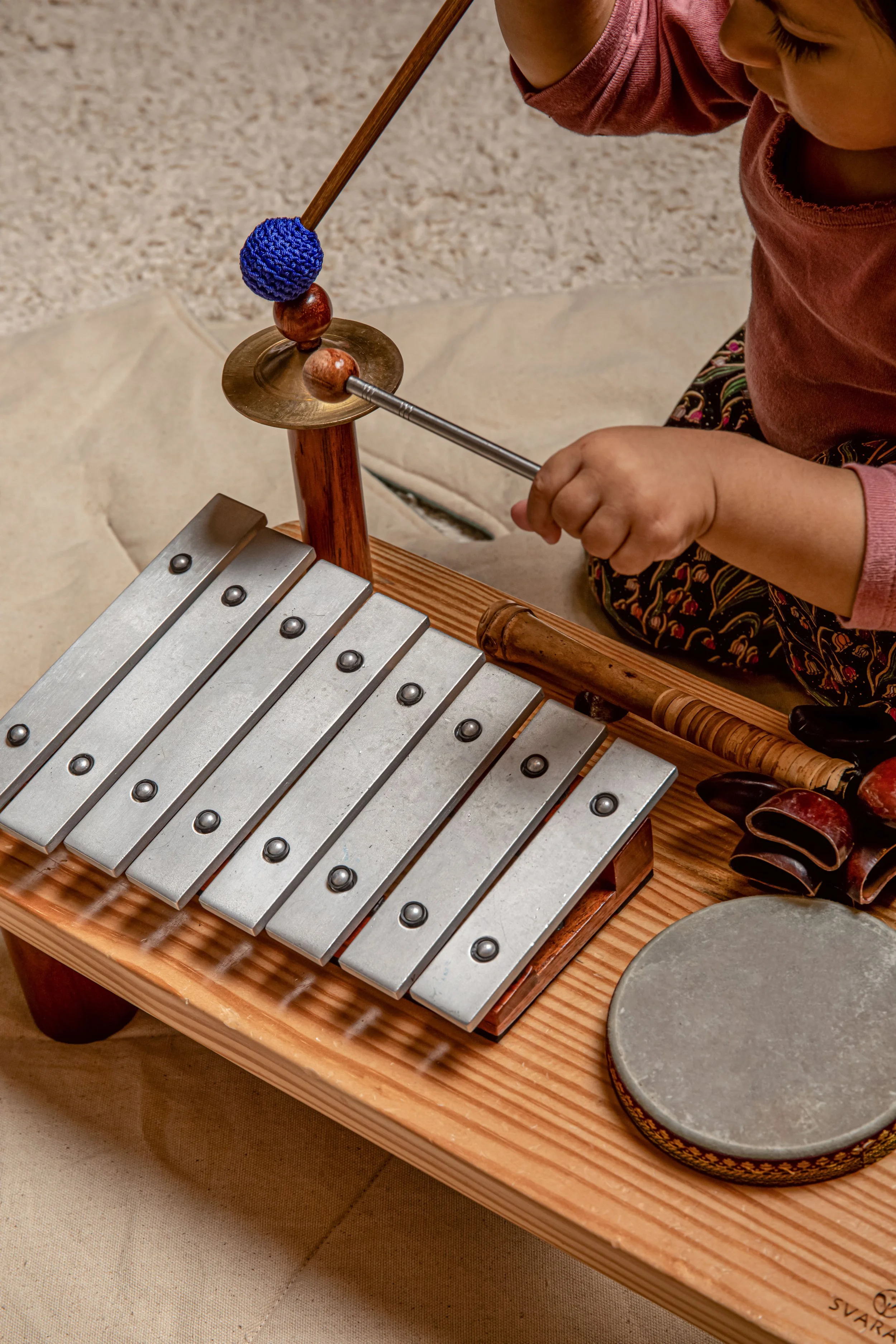 Child playing a small xylophone with metal bars on a wooden stand.