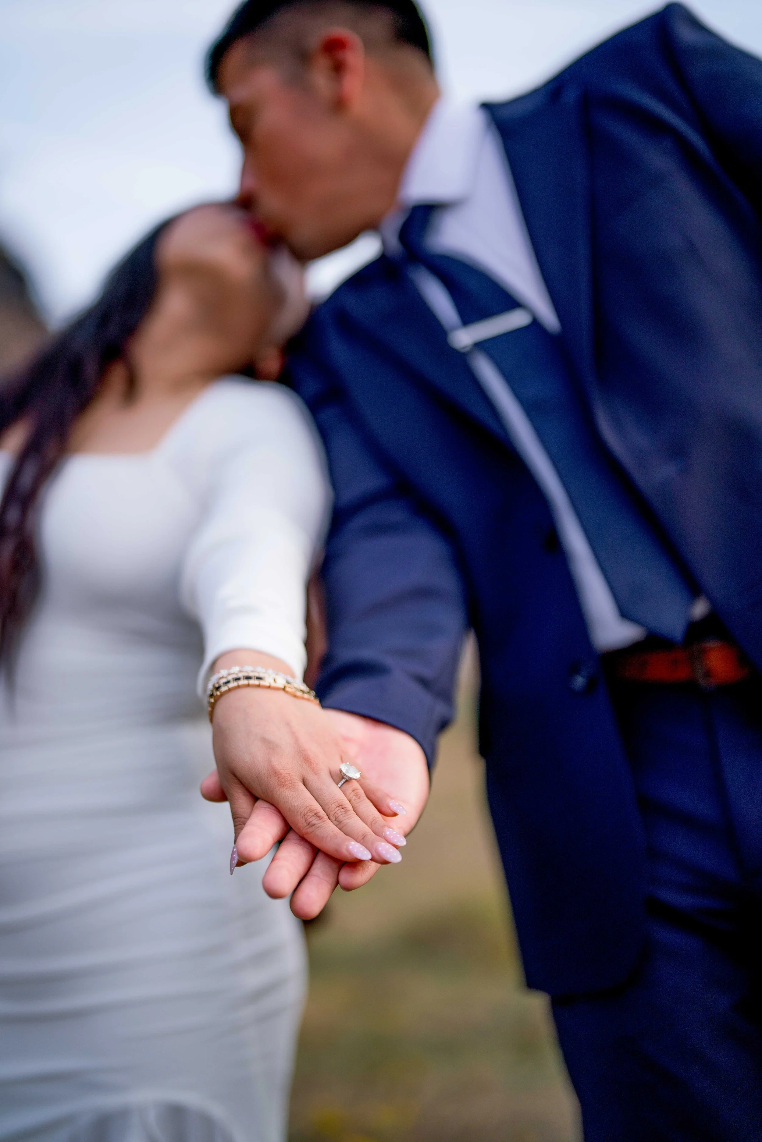 A couple holding hands with wedding rings, kissing in the background