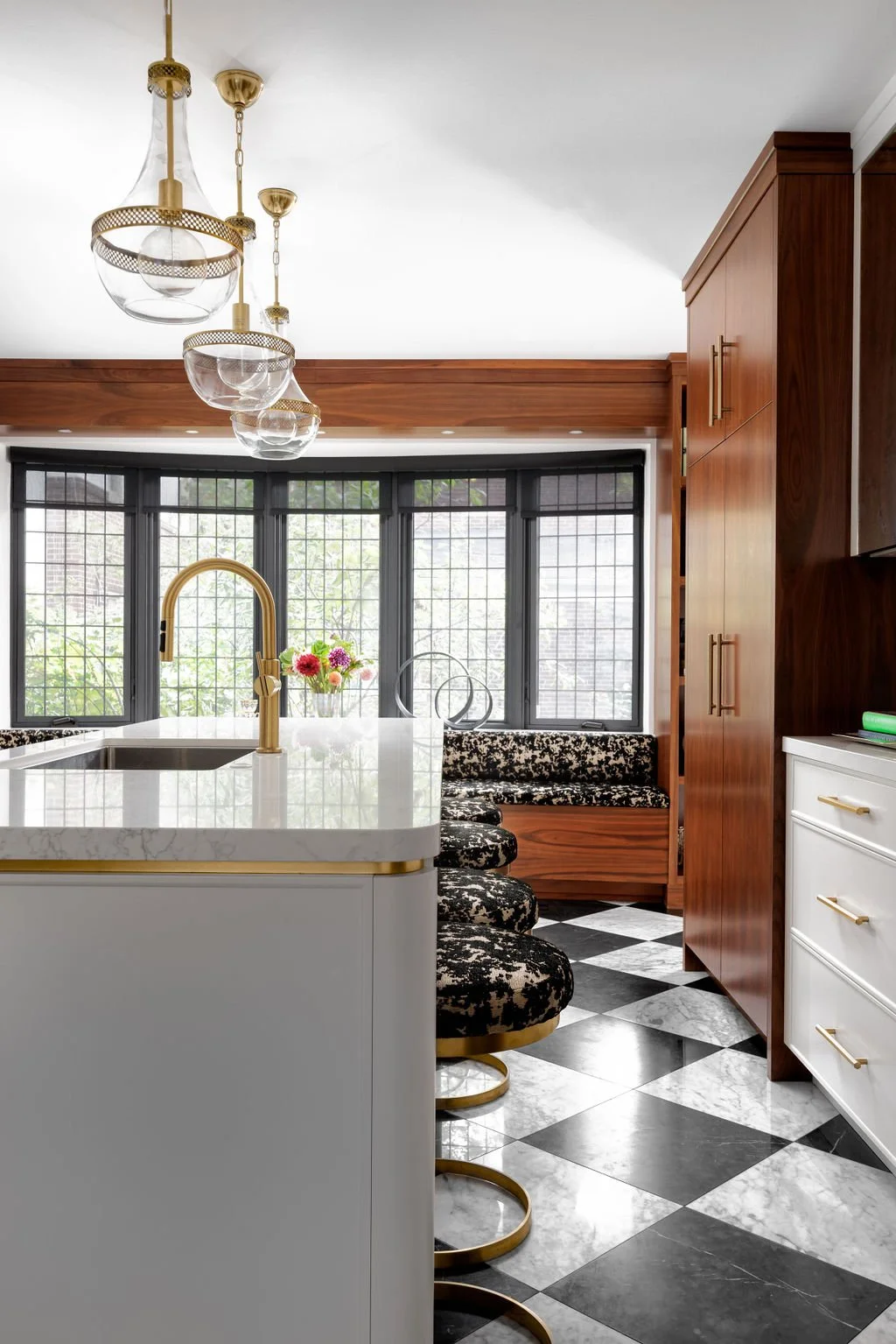 Modern kitchen with white quartz island, gold faucet, black and white checkered marble floor, dark wood cabinetry, and large bay windows with caming glass